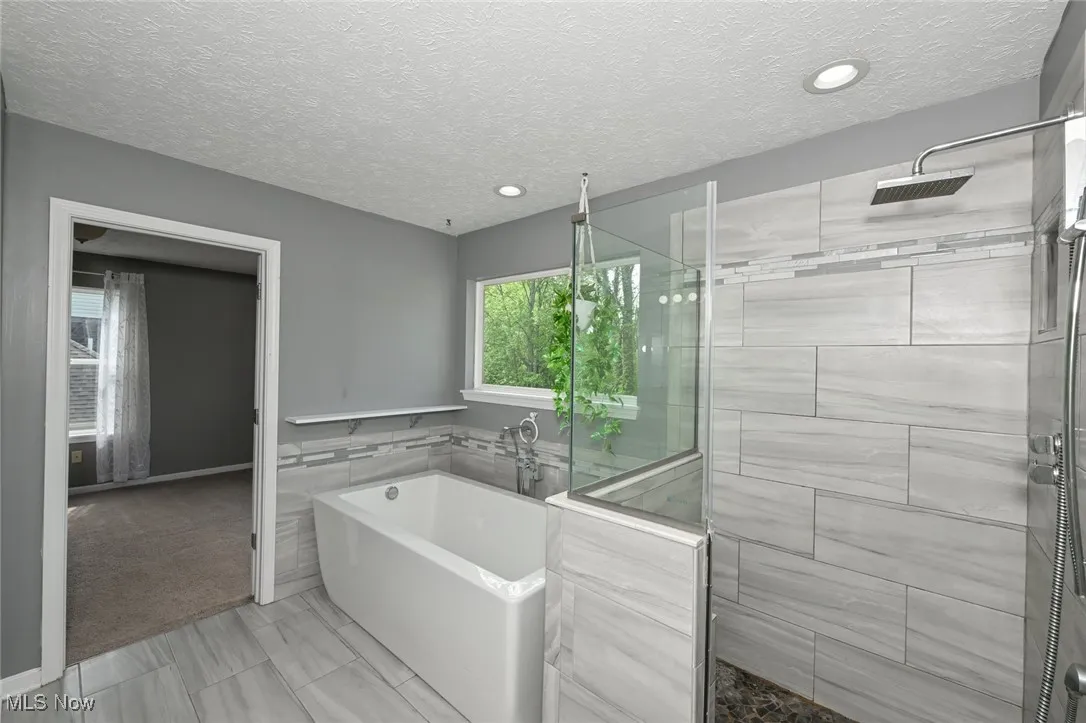Full updated bath with a tile shower, a bath, a textured ceiling, and recessed lighting