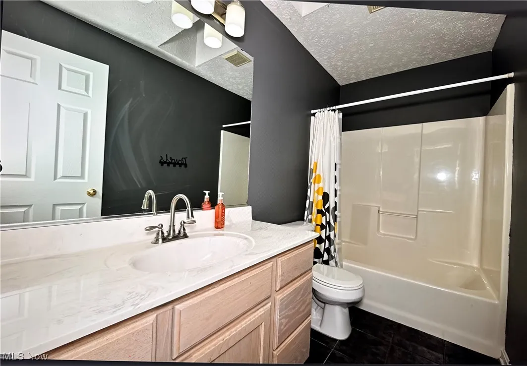 Bathroom featuring tile patterned floors, vanity, toilet, shower / bath combo with shower curtain, and a textured ceiling