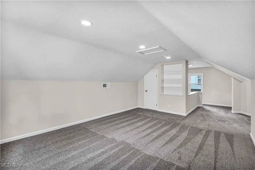 Additional living space with baseboards, attic access, dark colored carpet, lofted ceiling, and recessed lighting