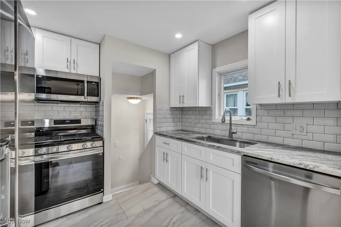 Kitchen featuring appliances with stainless steel finishes, a sink, light stone countertops, light marble finish floors, and white cabinets