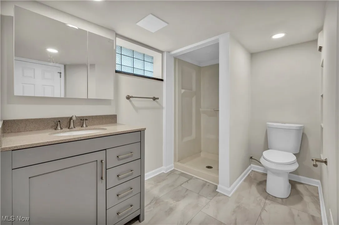 Full bathroom with baseboards, a stall shower, toilet, marble look tile flooring, and vanity