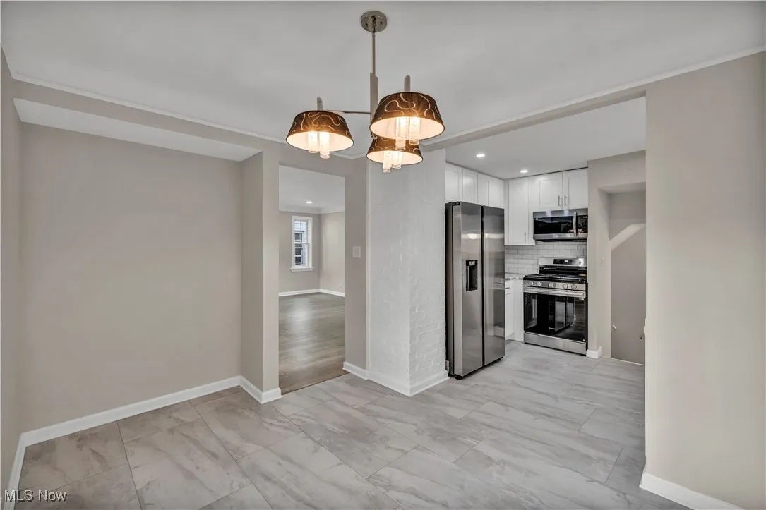 Kitchen featuring stainless steel appliances, light marble finish floors, white cabinets, backsplash, and baseboards
