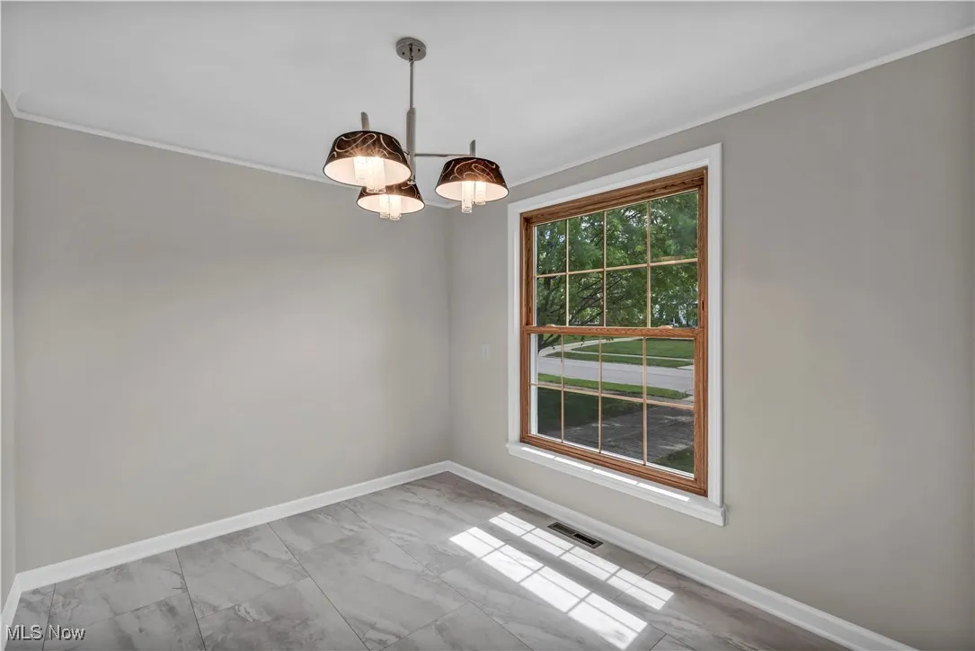 Unfurnished room featuring ornamental molding, marble finish floors, and baseboards