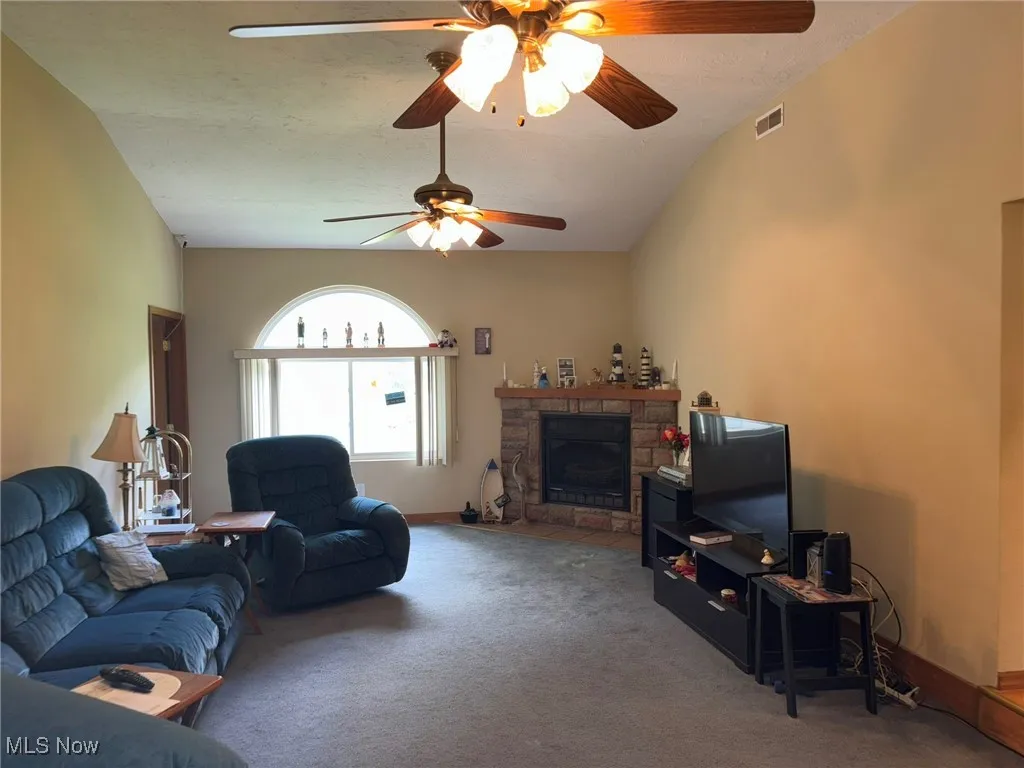 Living area featuring carpet flooring, a stone fireplace, and a ceiling fan