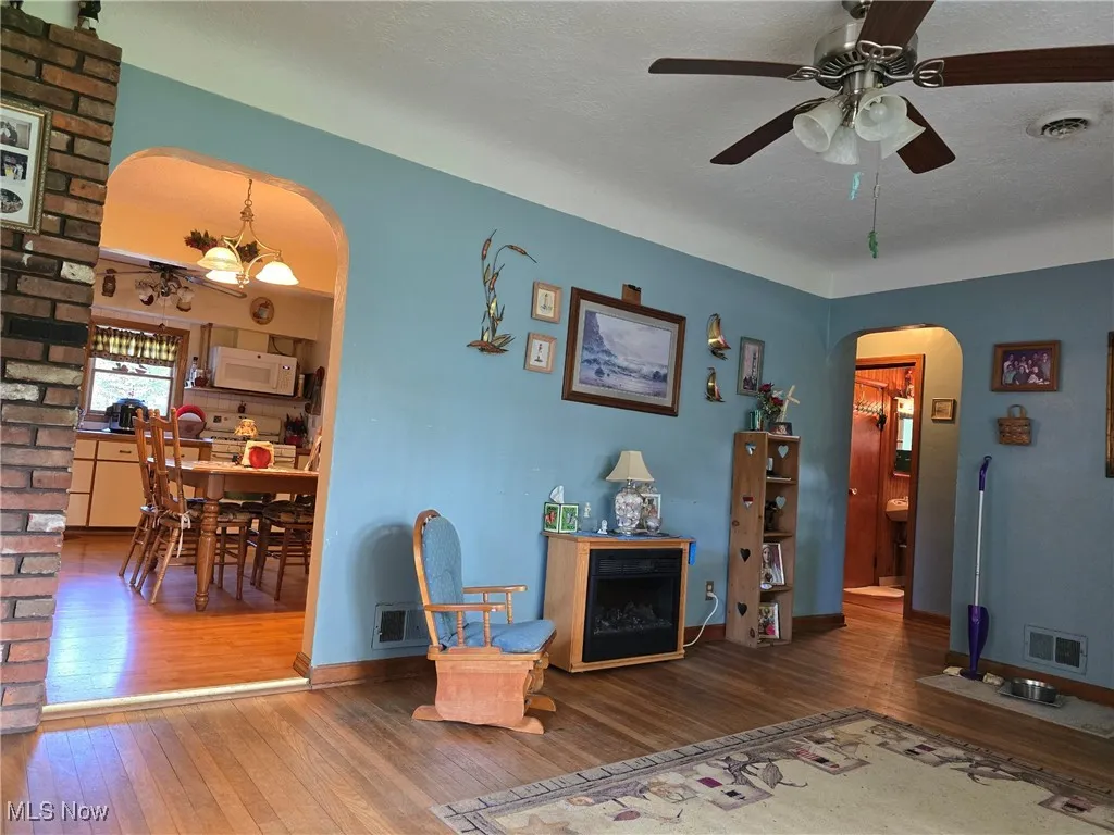 Living room featuring arched walkways, hardwood / wood-style floors, a ceiling fan, and baseboards