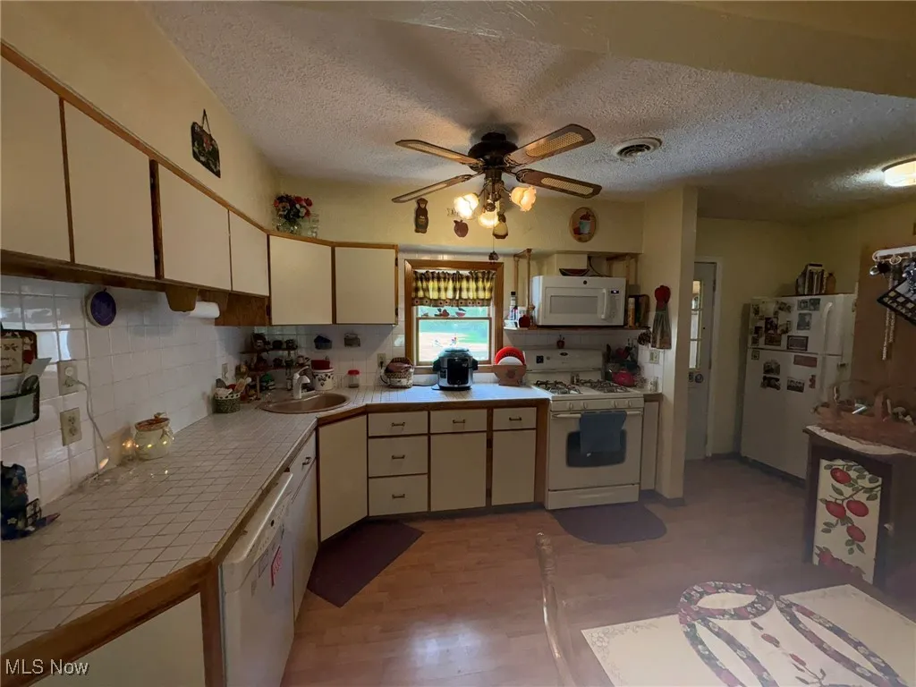 Kitchen with white appliances, tile countertops, a sink, a ceiling fan, and a textured ceiling