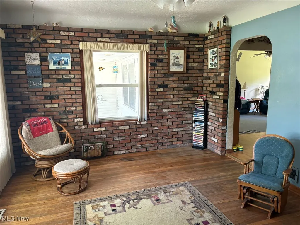 Living area featuring wood finished floors, ceiling fan, arched walkways, a textured ceiling, and brick wall