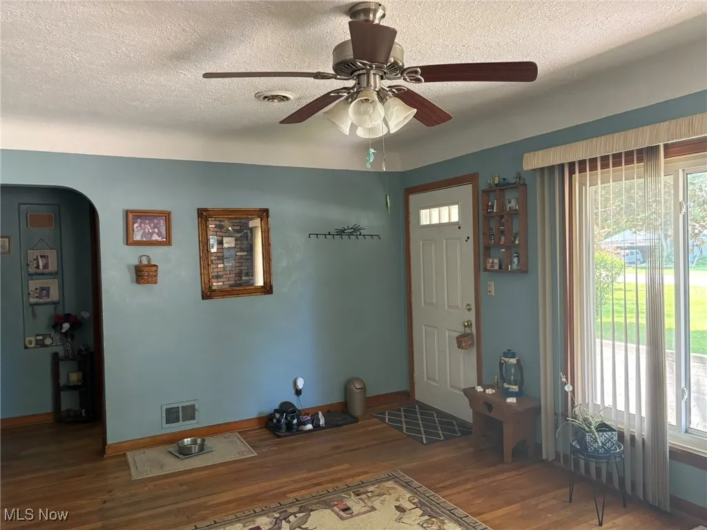 Foyer featuring wood finished floors, ceiling fan, baseboards, a textured ceiling, and arched walkways