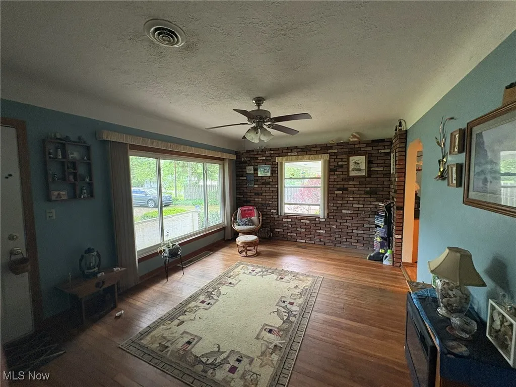 Living room with brick wall, a textured ceiling, a ceiling fan, and wood-type flooring