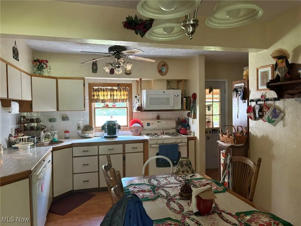 Kitchen featuring white appliances, backsplash, a ceiling fan, light wood-style floors, and tile counters
