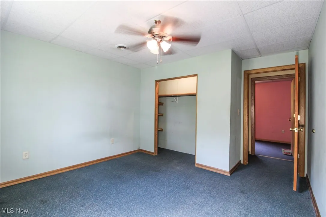 Unfurnished bedroom featuring carpet, baseboards, a drop ceiling, a ceiling fan, and a closet