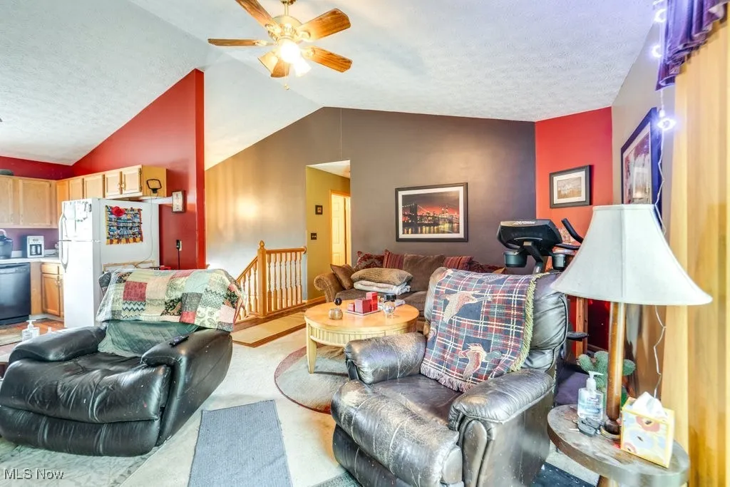 Living area with lofted ceiling, a ceiling fan, and a textured ceiling