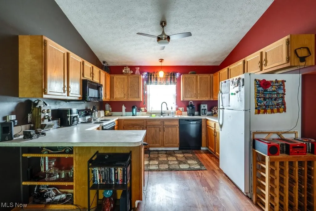 Kitchen featuring black appliances, a sink, light wood finished floors, lofted ceiling, and a textured ceiling