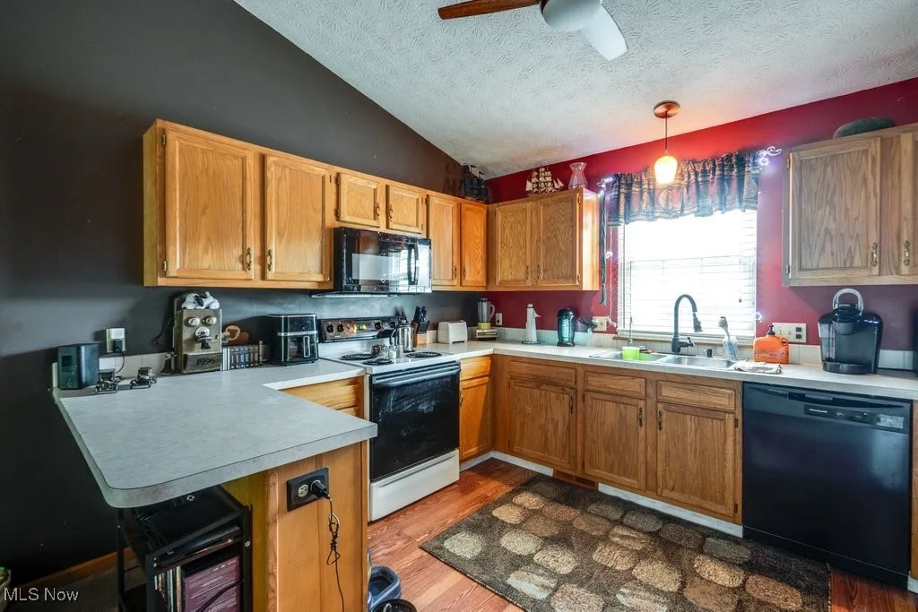 Kitchen featuring black appliances, a sink, a textured ceiling, a peninsula, and light countertops