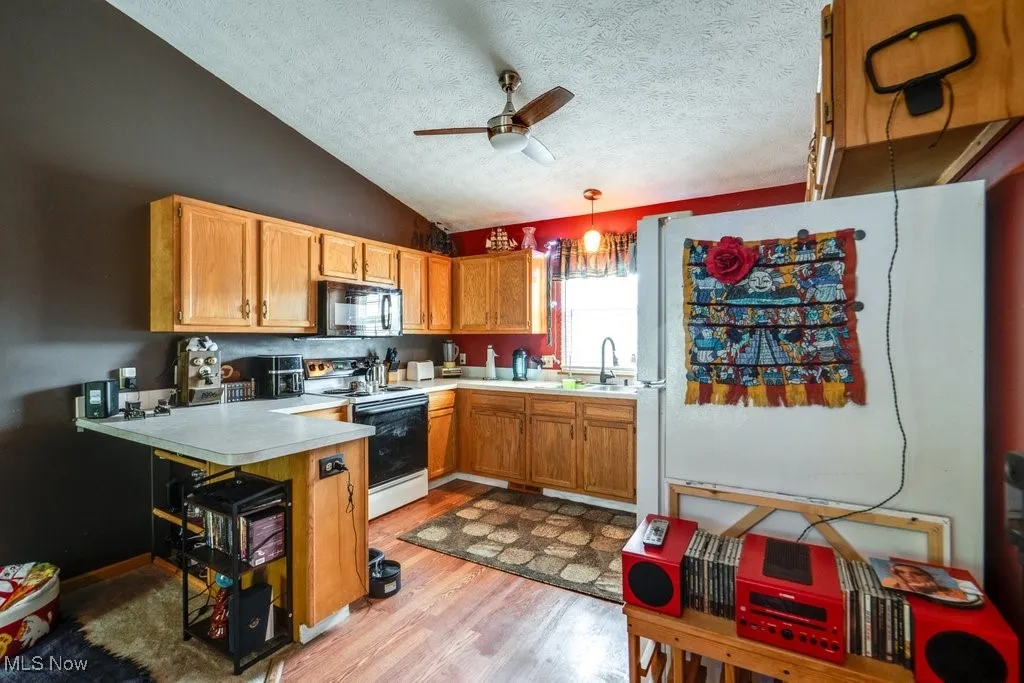 Kitchen featuring range with electric stovetop, black microwave, a ceiling fan, light wood-style floors, and light countertops