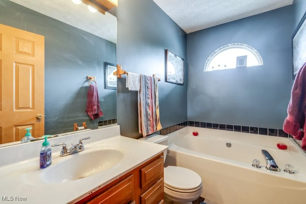 Bathroom with a garden tub, a textured ceiling, vanity, and toilet