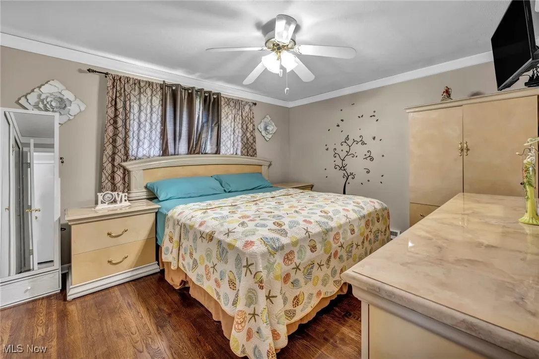 Bedroom with dark wood finished floors, ornamental molding, and a ceiling fan