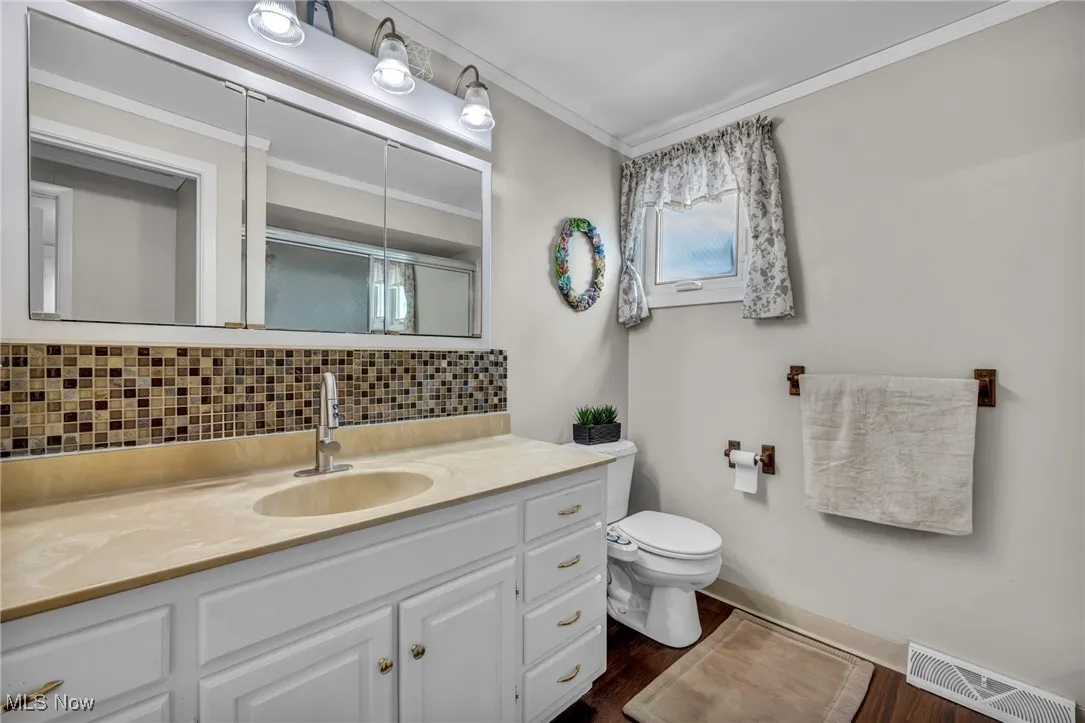 Full bath featuring tasteful backsplash, wood finished floors, toilet, vanity, and crown molding