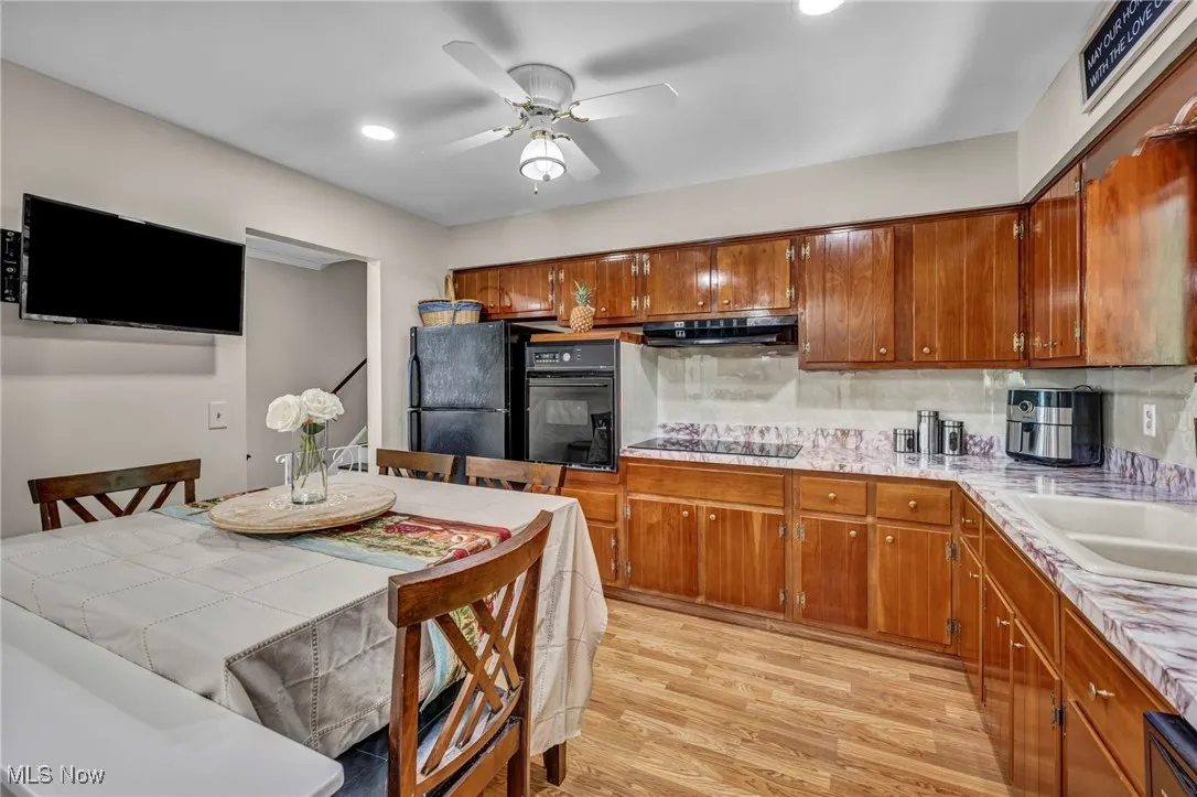 Kitchen with black appliances, under cabinet range hood, brown cabinetry, decorative backsplash, and light wood-style floors