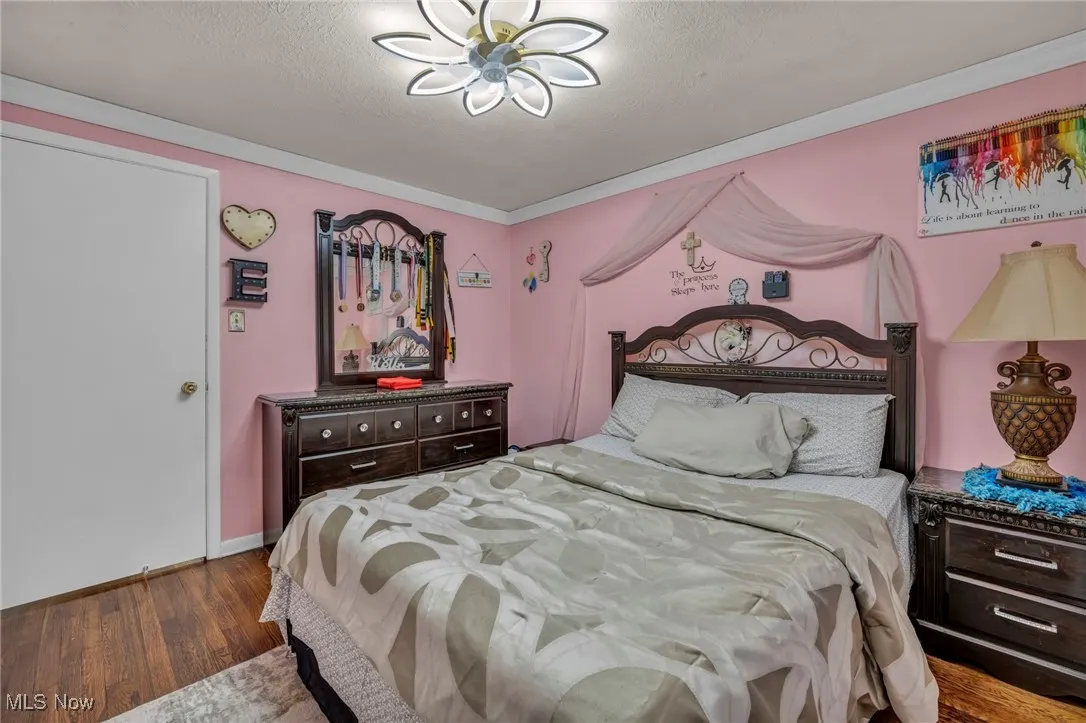 Bedroom featuring wood finished floors, a textured ceiling, baseboards, and crown molding