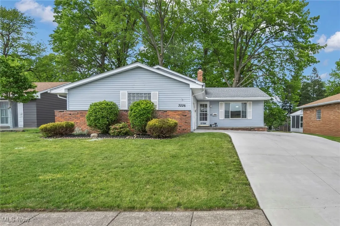 Ranch-style house with driveway, brick siding, a chimney, and a front lawn