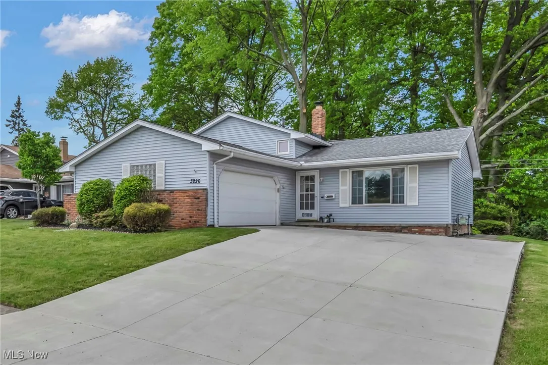 View of front facade featuring driveway, a chimney, a garage, a front lawn, and brick siding