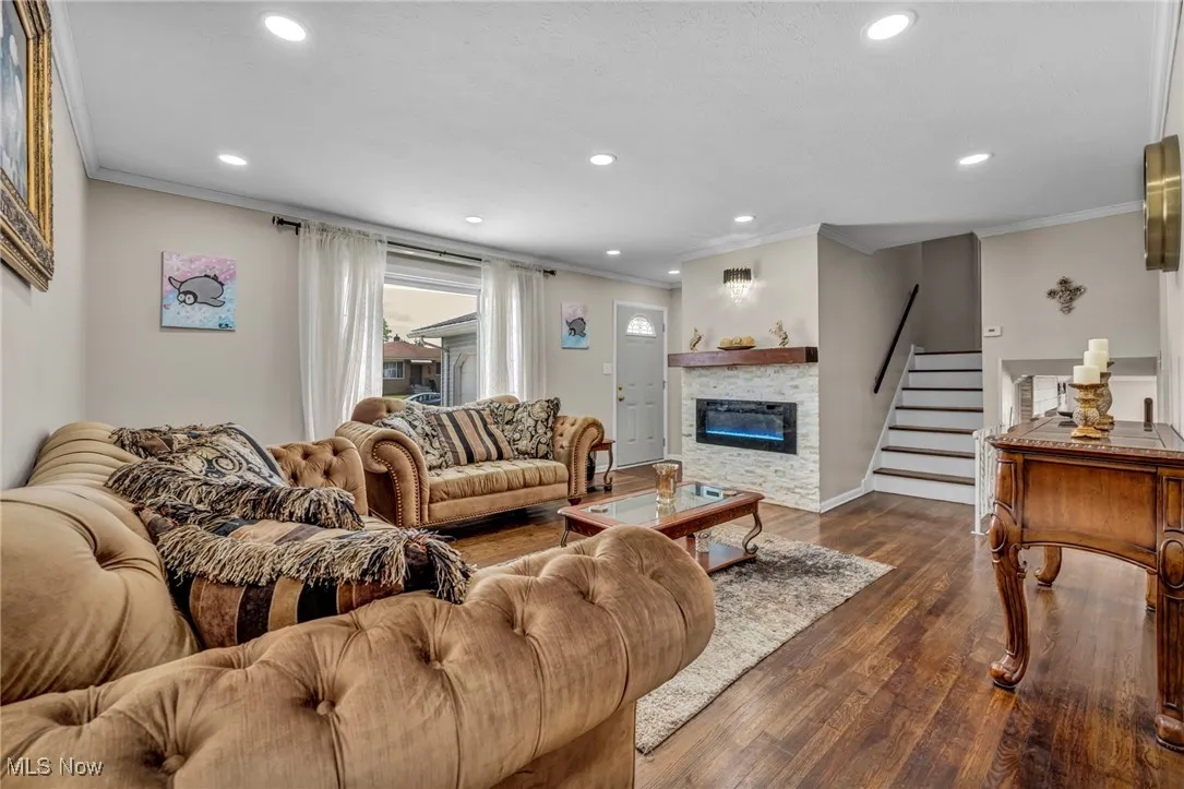 Living room with crown molding, recessed lighting, dark wood finished floors, a stone fireplace, and stairway