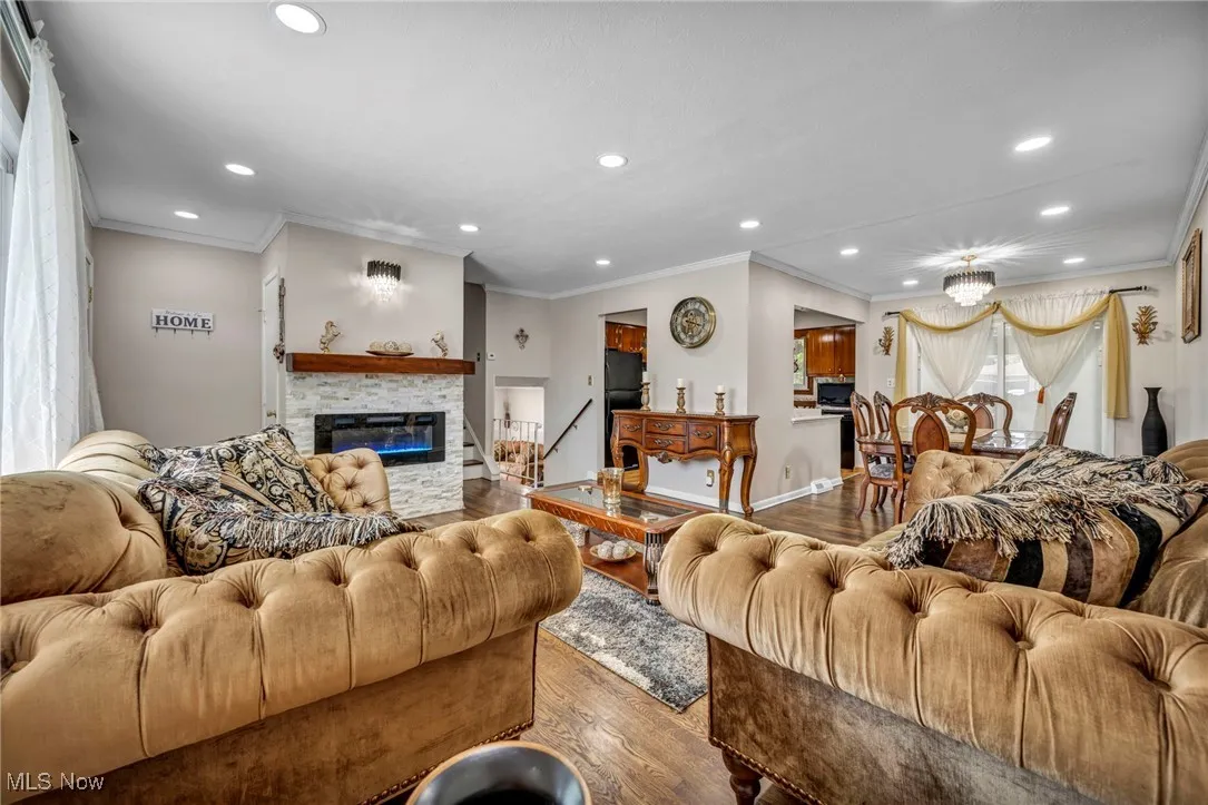 Living room featuring wood finished floors, recessed lighting, crown molding, and a stone fireplace