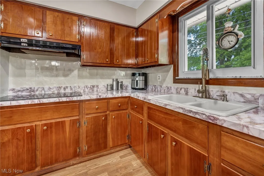 Kitchen with a sink, light countertops, black electric cooktop, and brown cabinetry