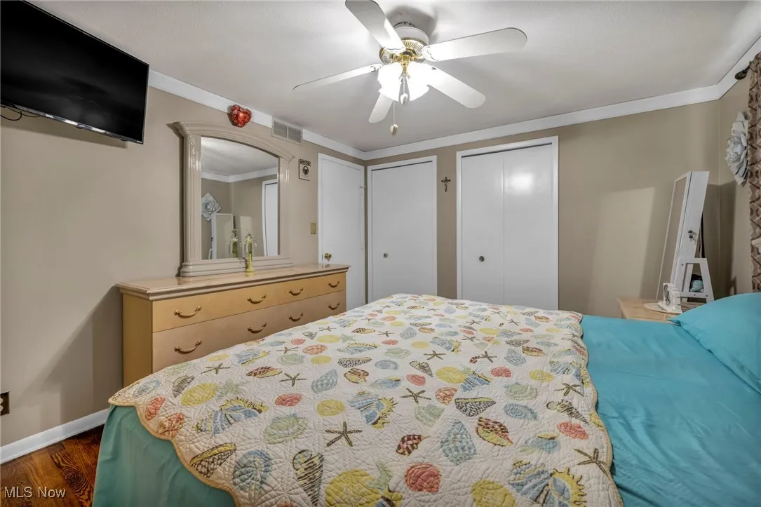Bedroom featuring two closets, dark wood-style floors, baseboards, a ceiling fan, and arched walkways