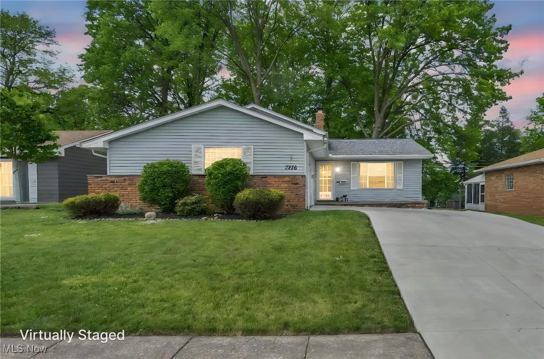 Single story home featuring a chimney, driveway, a lawn, and brick siding