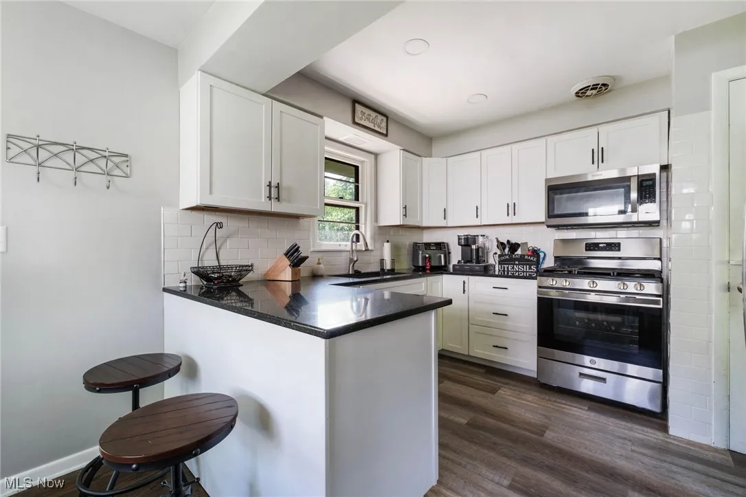 Kitchen with stainless steel appliances, a sink, a peninsula, white cabinets, and dark wood-style floors