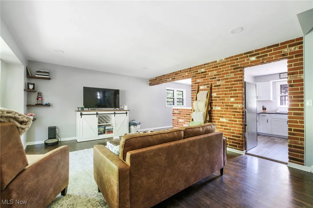 Living area featuring healthy amount of natural light, brick wall, dark wood-style flooring, and baseboards