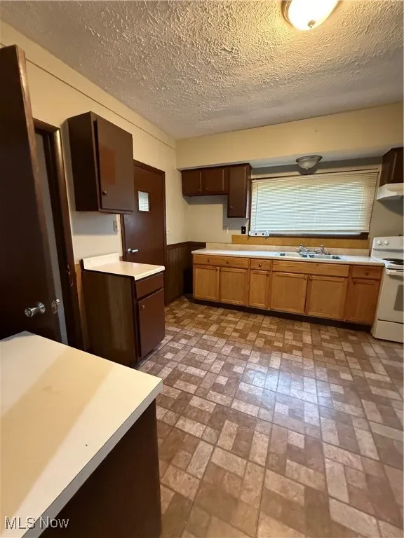 Kitchen featuring range, a sink, wainscoting, exhaust hood, and brick patterned flooring