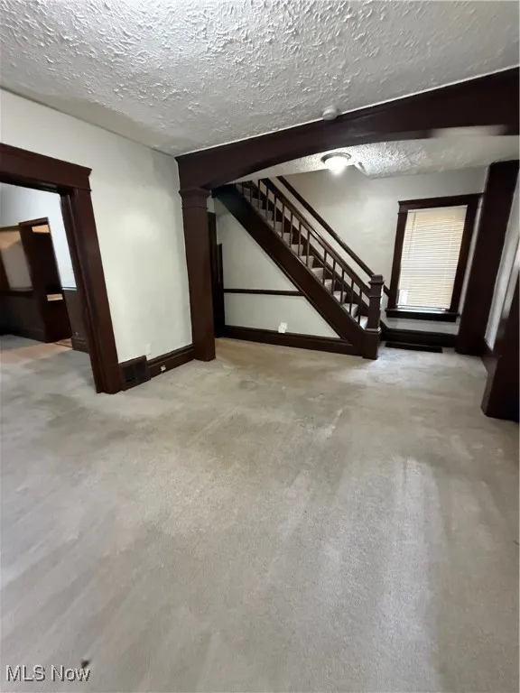 Basement with stairs, carpet, a textured ceiling, and baseboards