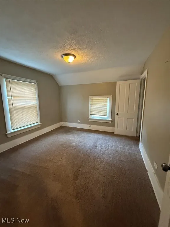 Carpeted spare room with vaulted ceiling, a textured ceiling, and baseboards