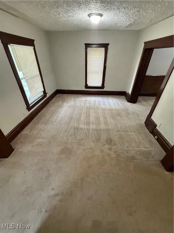 Empty room with light colored carpet, a textured ceiling, and baseboards