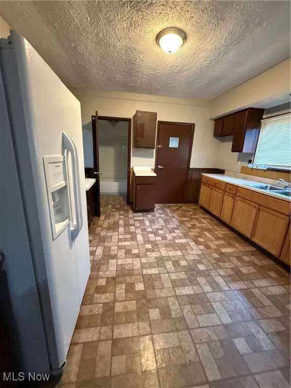 Kitchen featuring fridge, brick patterned flooring, a sink, a textured ceiling, and light countertops
