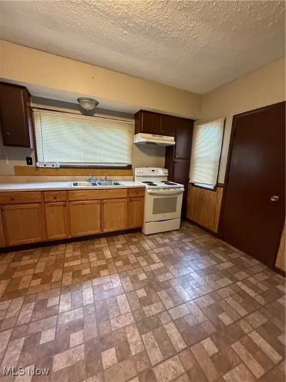 Kitchen featuring white electric range, ventilation hood, brick patterned floors, a sink, and light countertops