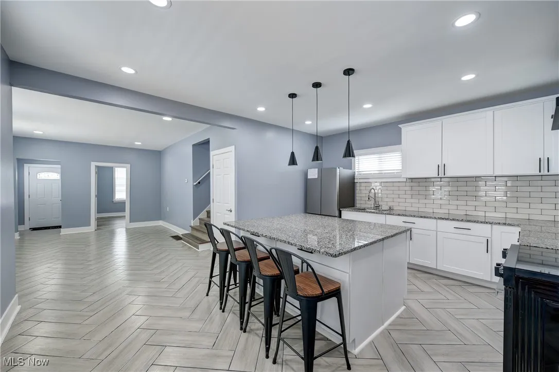 Kitchen featuring freestanding refrigerator, baseboards, a sink, a center island, and recessed lighting