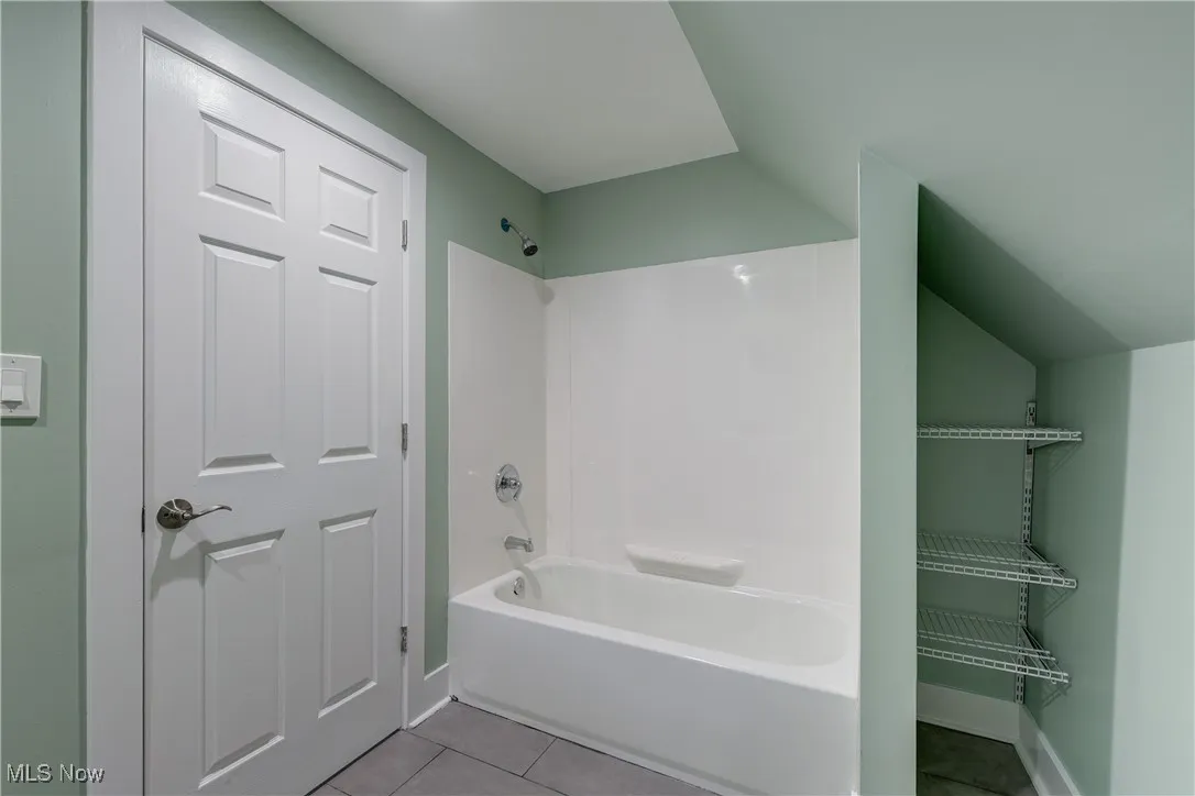Full bath featuring tile patterned flooring, vaulted ceiling, baseboards, and washtub / shower combination