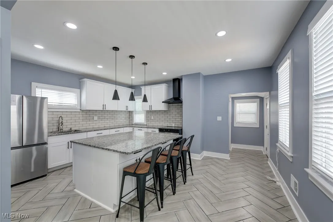 Kitchen with freestanding refrigerator, wall chimney range hood, a sink, a center island, and tasteful backsplash