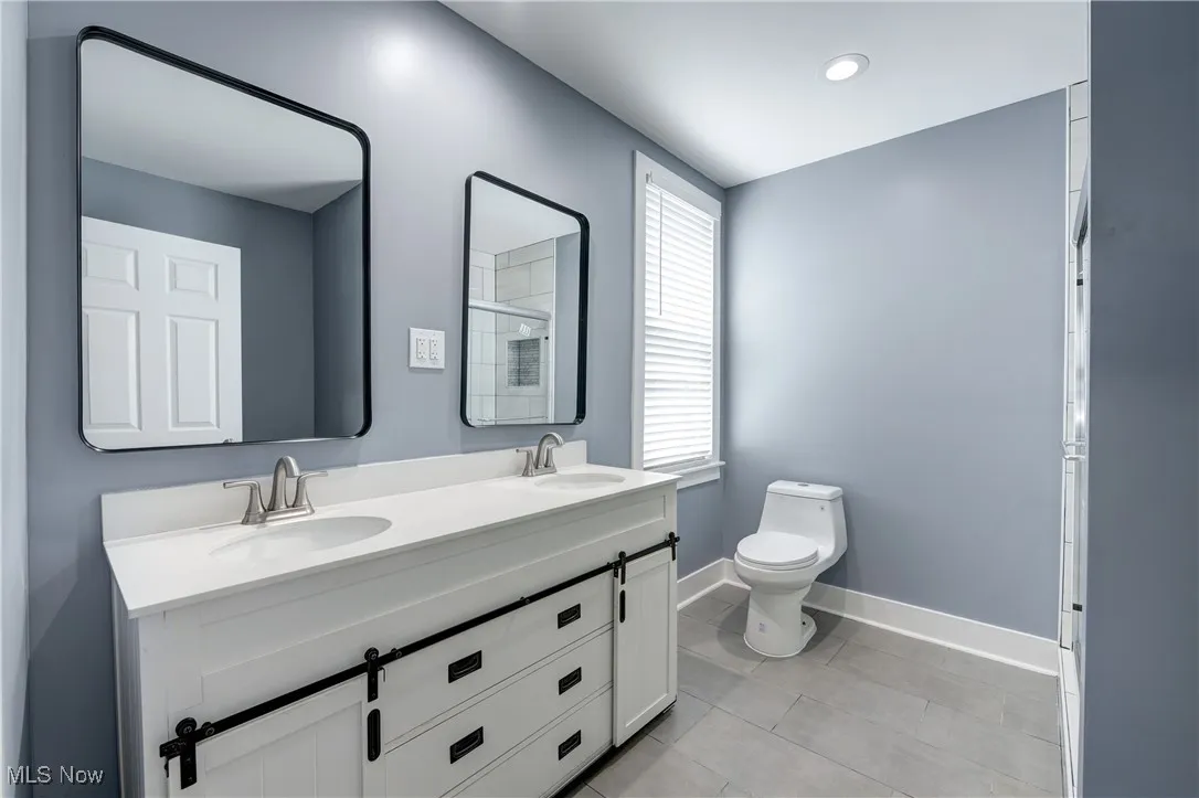 Bathroom featuring baseboards, toilet, an enclosed shower, double vanity, and tile patterned floors