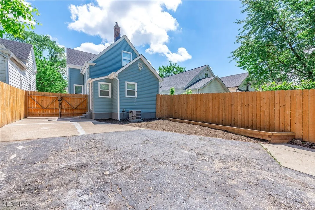 Rear view of property featuring central AC, a chimney, a fenced backyard, asphalt driveway, and a gate