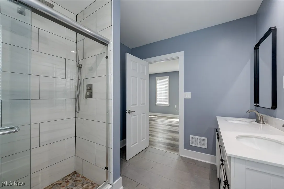 Bathroom featuring baseboards, a stall shower, double vanity, and tile patterned floors