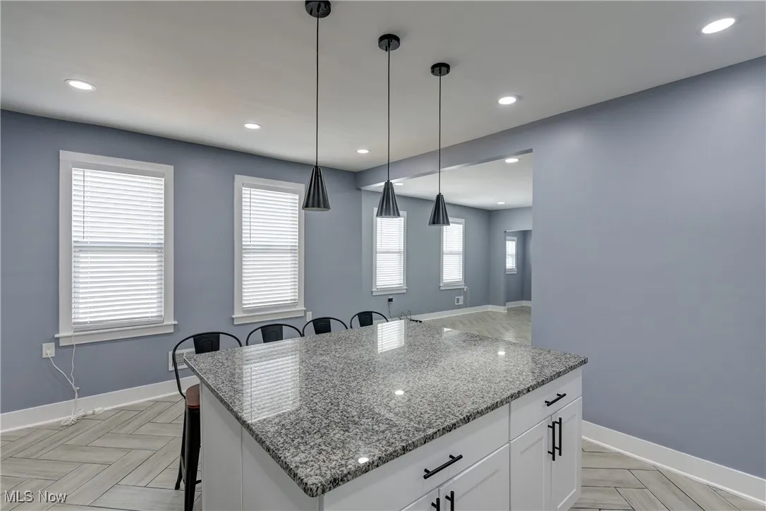 Kitchen with a kitchen island, a kitchen breakfast bar, white cabinets, decorative light fixtures, and light stone counters