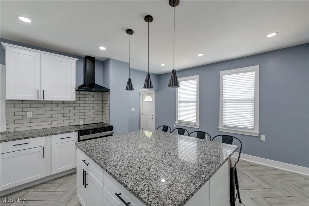 Kitchen with wall chimney range hood, electric range, a breakfast bar, tasteful backsplash, and a kitchen island