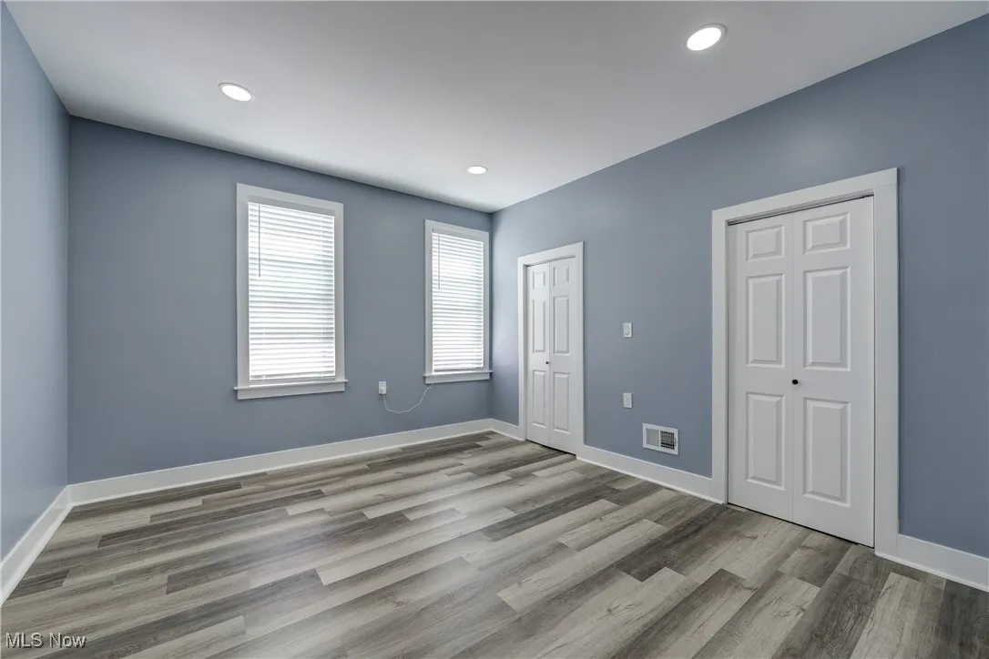 Unfurnished bedroom with wood finished floors, baseboards, recessed lighting, and two closets