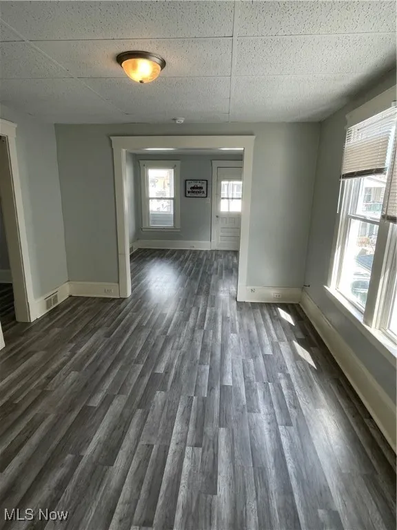 Empty room featuring baseboards, dark wood-style flooring, and a drop ceiling