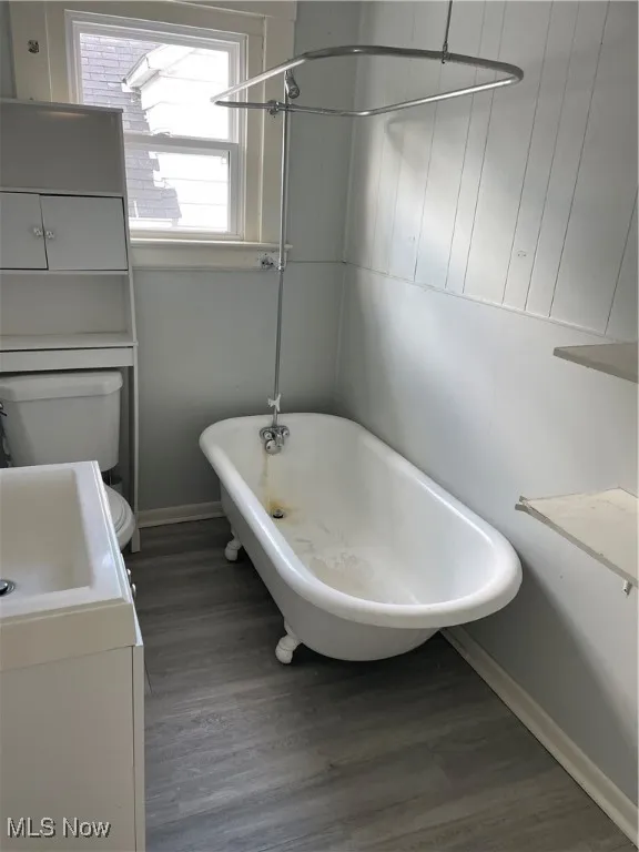 Full bath featuring wood finished floors, a freestanding tub, baseboards, vanity, and toilet